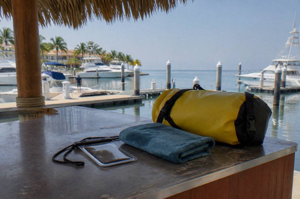 Yellow dry bag, blue towel and waterproof phone pouch on a counter overlooking a marina