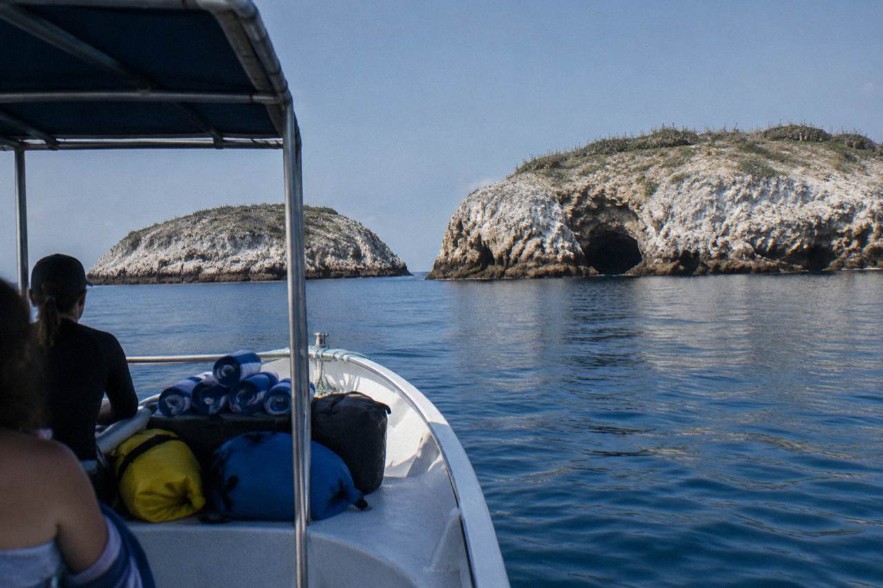 Rolled towels and dry bags on a small boat approaching rocky islands with a sea cave