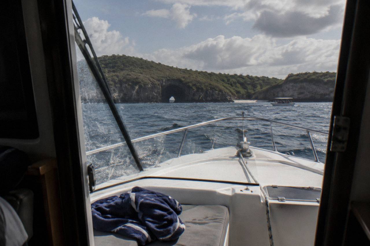 View from inside a boat cabin toward a rocky arch island, towel on bow seat